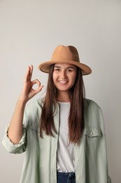 Smiling young woman showing okay gesture in stylish outfit on light background