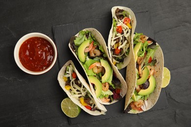 Photo of Delicious tacos, lime and sauce on black table, flat lay