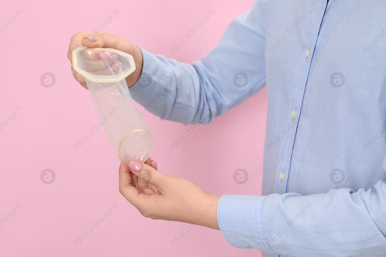 Photo of Woman with unrolled female condom on pink background, closeup. Safe sex