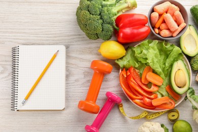 Photo of Healthy diet. Fresh vegetables, notebook, dumbbells, pencil and measuring tape on light wooden table, flat lay