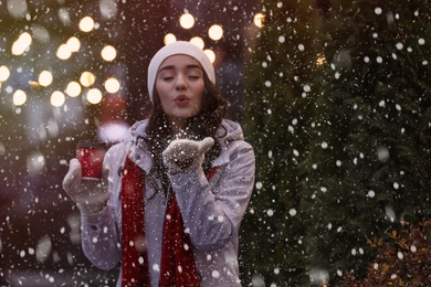 Happy young woman with cup of drink on city street in evening. Christmas celebration