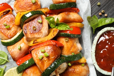 Photo of Delicious chicken shish kebabs with vegetables and ketchup on black table, closeup