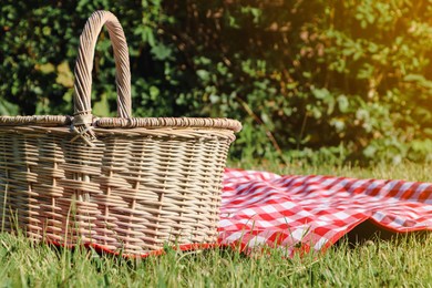 Photo of Picnic basket with checkered tablecloth on green grass outdoors, space for text