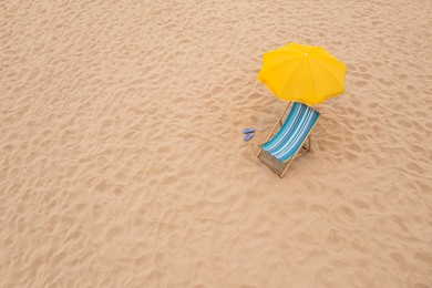 Image of Yellow beach umbrella, sunbed and flip flops on sandy coast. Space for text