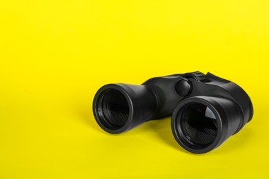 Photo of Modern binoculars on yellow background, space for text
