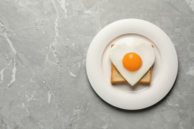 Photo of Plate with tasty fried egg in shape of heart and toast on marble table, top view. Space for text