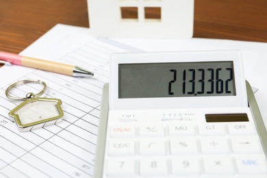 Calculator, house shaped trinket, pen and documents on table. Real estate agent's workplace