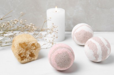 Photo of Bath bombs, loofah sponge and burning candle on white table