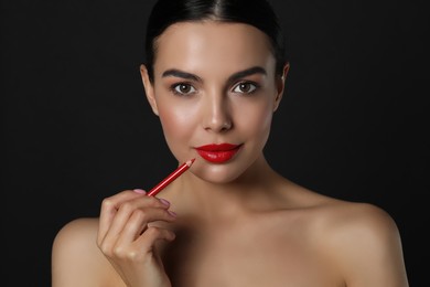 Photo of Pretty young woman with beautiful red lip pencil on black background