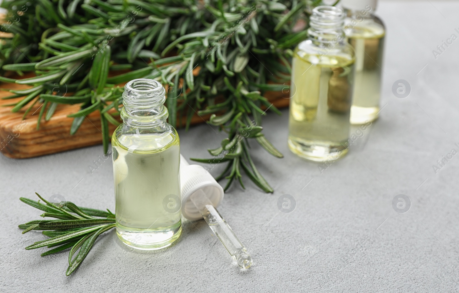 Photo of Fresh rosemary and bottle of essential oil on light grey table. Space or text