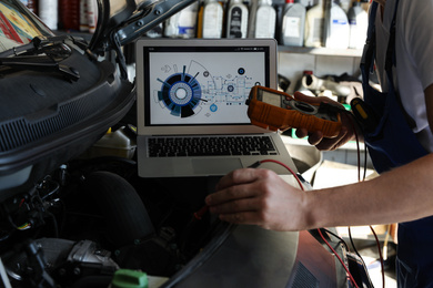 Photo of Mechanic with laptop doing car diagnostic at automobile repair shop, closeup