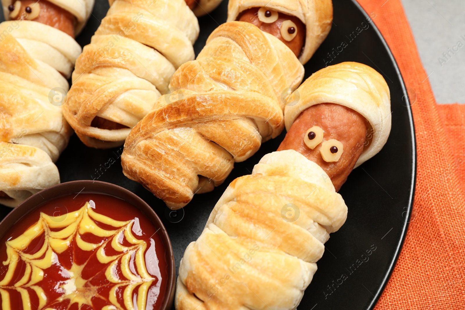 Photo of Spooky sausage mummies and sauce for Halloween party on plate, closeup