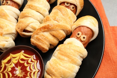 Photo of Spooky sausage mummies and sauce for Halloween party on plate, closeup