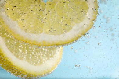 Photo of Juicy lemon slices in soda water against light blue background, closeup