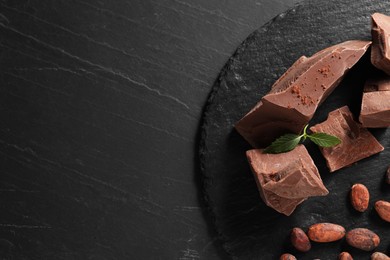 Pieces of tasty milk chocolate, cocoa beans, powder and mint on grey textured table, top view. Space for text