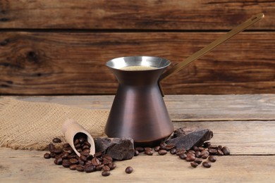Photo of Hot turkish coffee pot, beans and chocolate on wooden table