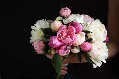 Woman with bouquet of beautiful peonies on black background, closeup