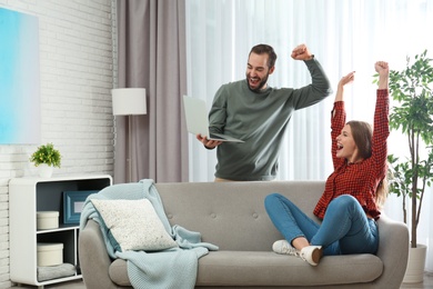 Photo of Emotional young couple with laptop celebrating victory at home