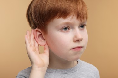 Little boy with hearing problem on pale brown background, closeup