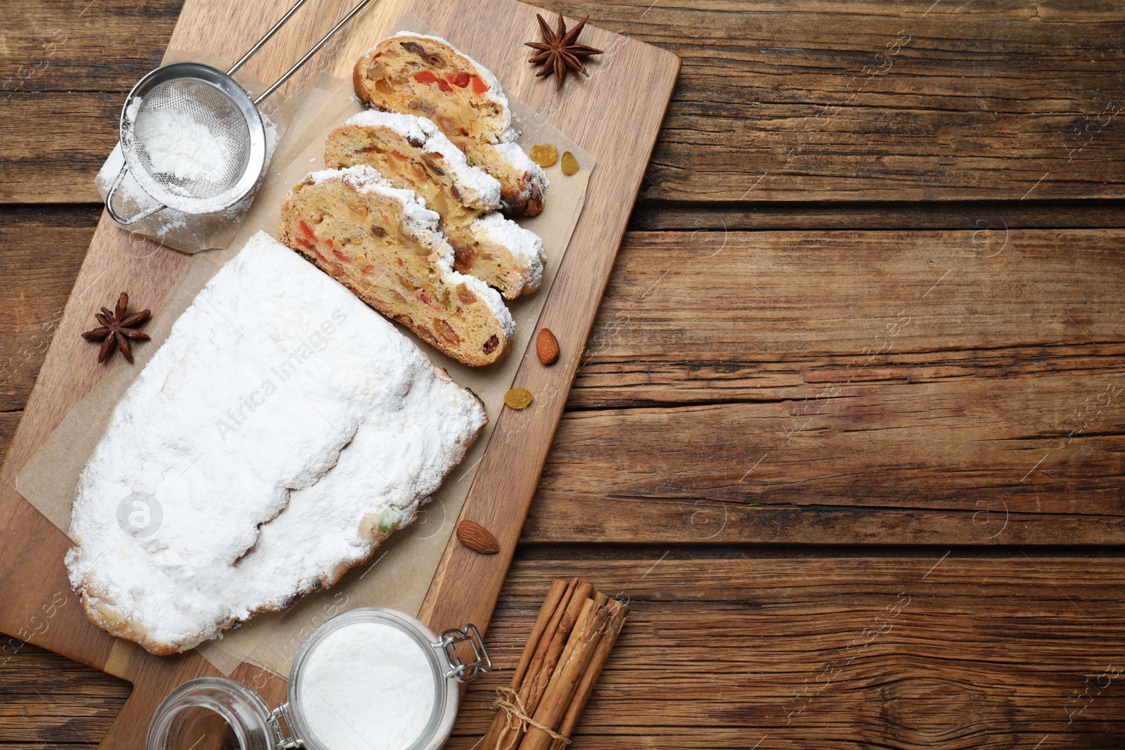 Photo of Traditional Christmas Stollen with icing sugar on wooden table, flat lay. Space for text