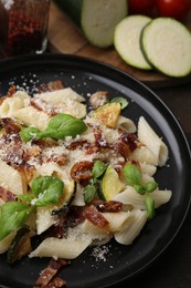 Tasty pasta with bacon and basil on wooden table, closeup