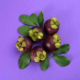 Photo of Fresh ripe mangosteen fruits with green leaves on violet background, flat lay