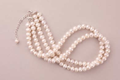 Elegant pearl necklace on beige background, top view