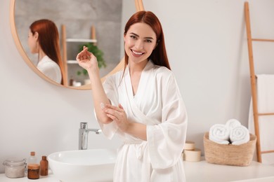 Photo of Beautiful young woman applying body cream onto elbow in bathroom