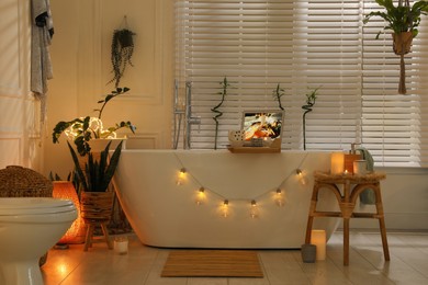 Photo of Stylish bathroom interior with green houseplants and string lights. Idea for design