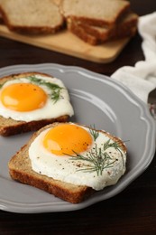 Photo of Plate with tasty fried eggs, slices of bread and dill on dark wooden table, closeup