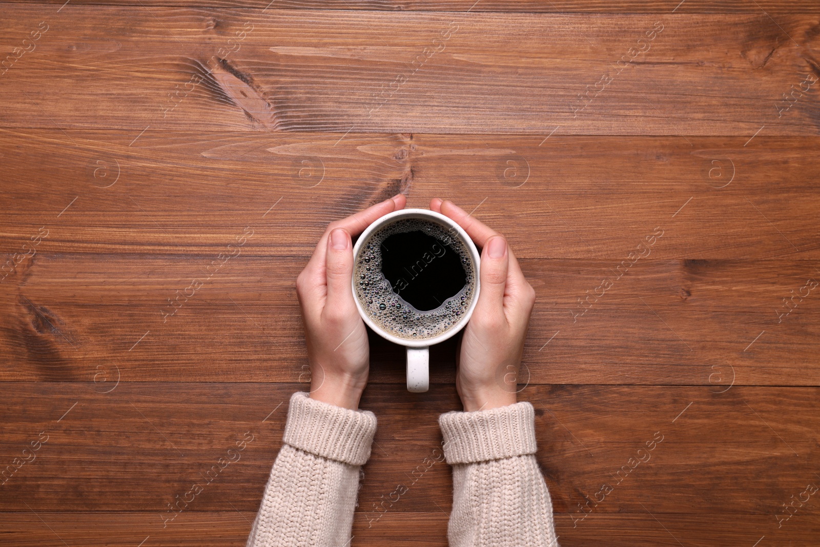 Photo of Woman with cup of coffee at wooden table, top view