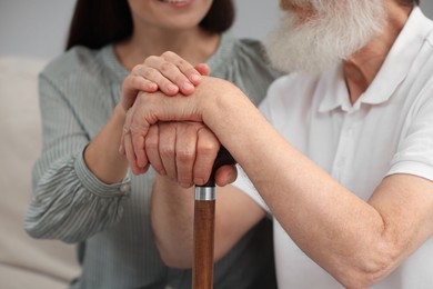 Senior man with walking cane and young woman indoors, closeup