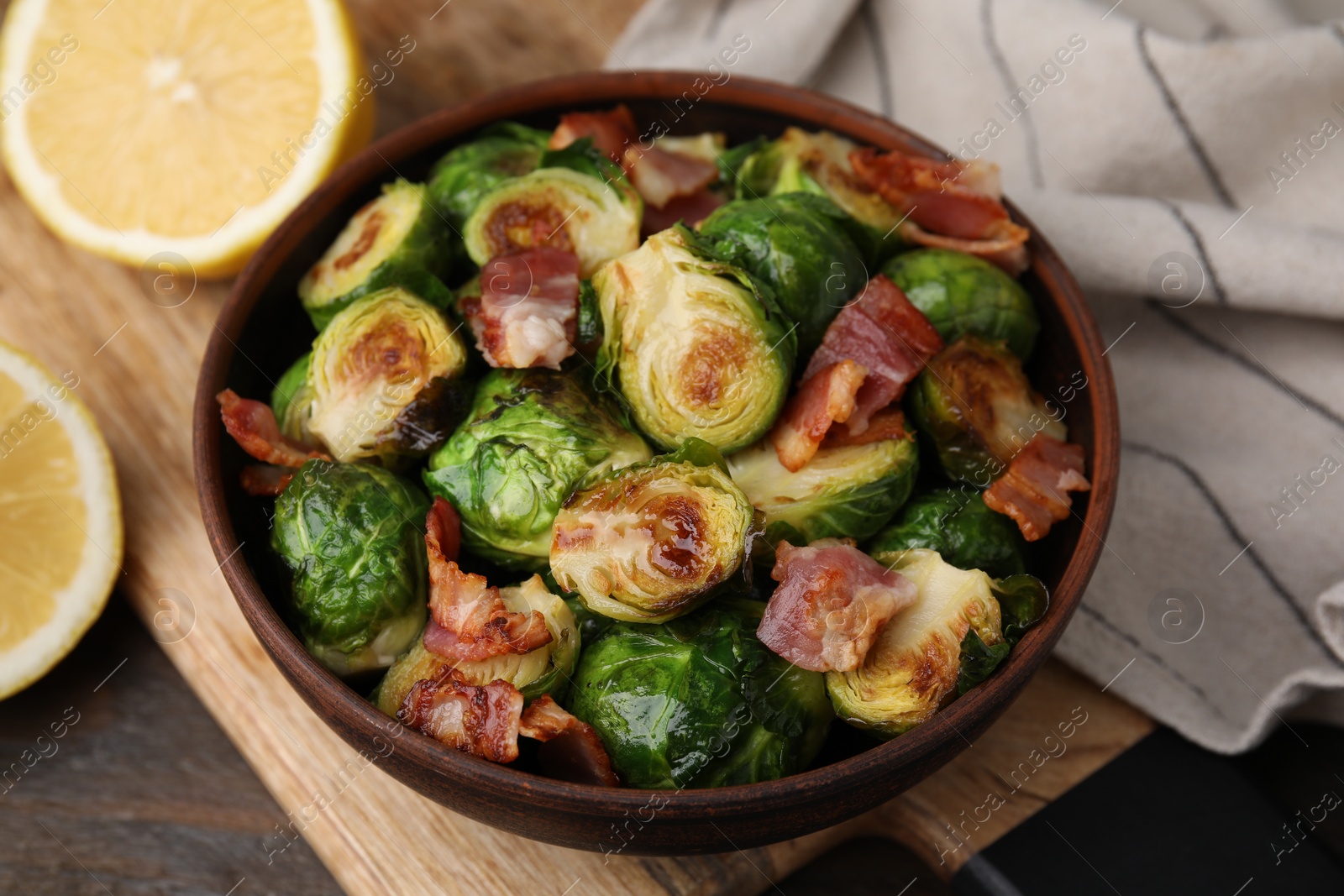 Photo of Delicious roasted Brussels sprouts and bacon in bowl on wooden table, closeup