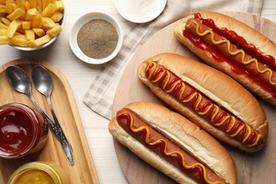 Photo of Fresh delicious hot dogs with sauces served on white wooden table, flat lay