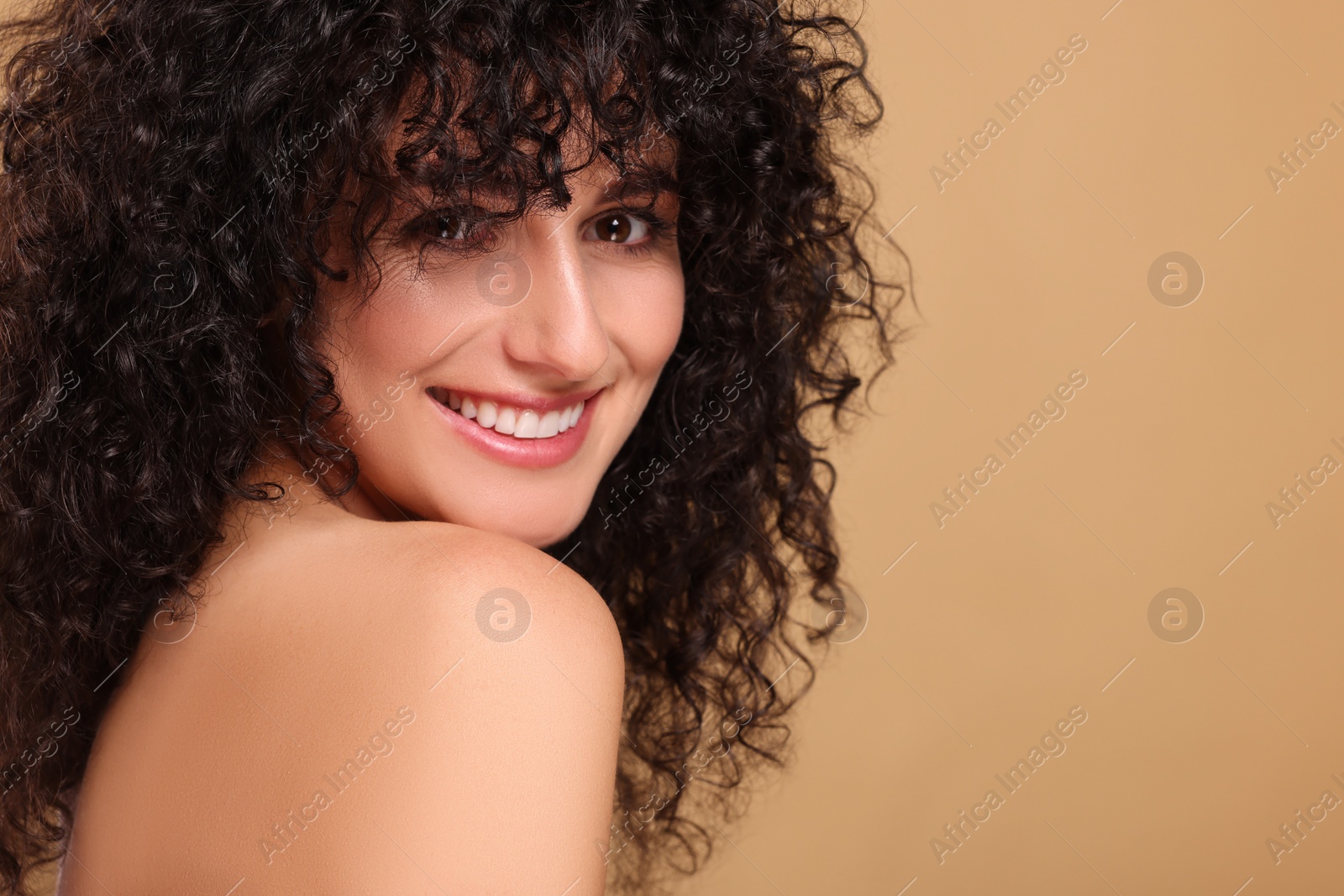 Photo of Beautiful young woman with long curly hair on beige background. Space for text