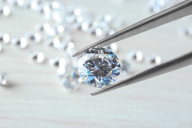 Tweezers with beautiful shiny diamond against light blurred background, closeup. Space for text