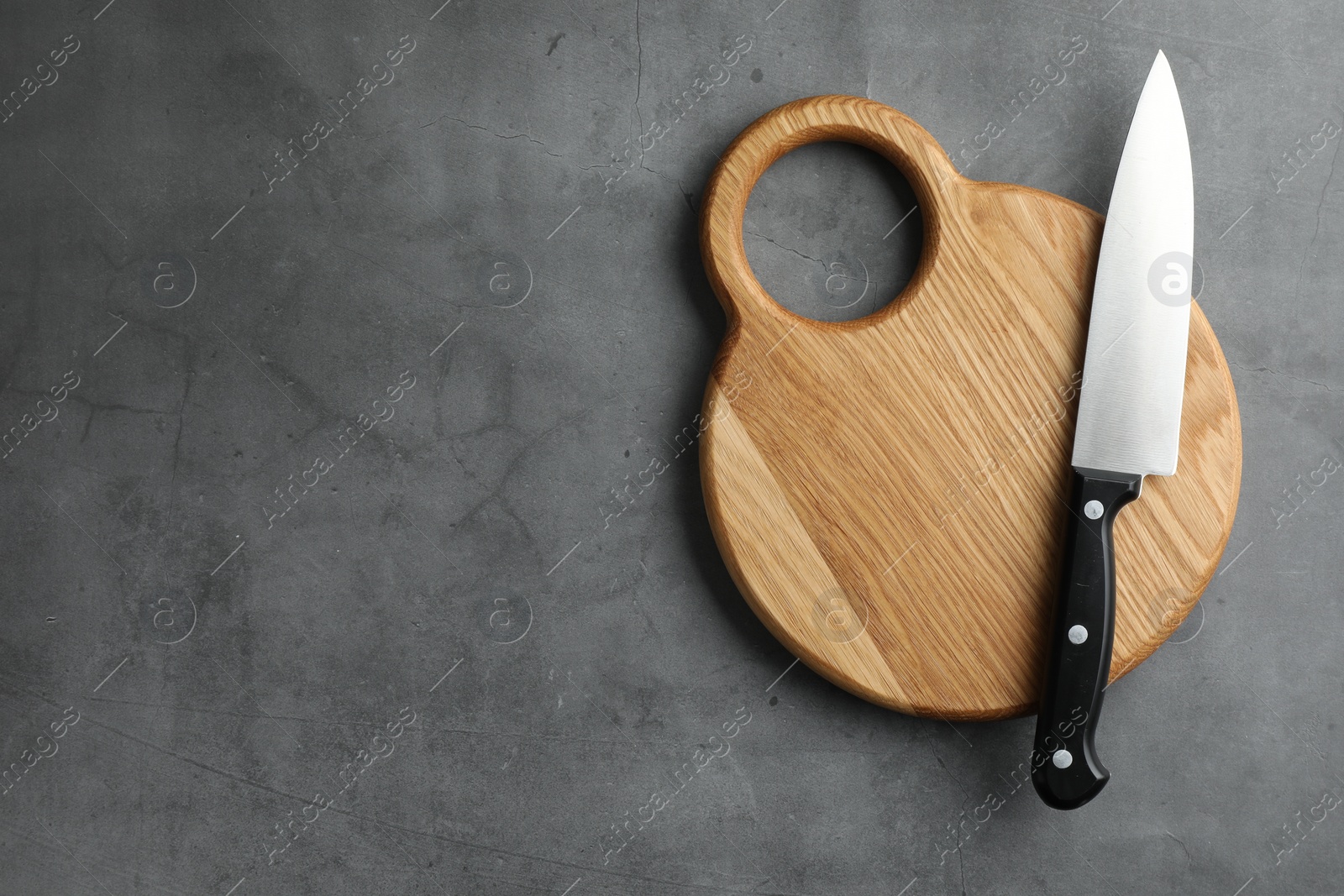 Photo of Knife and wooden board on grey textured table, top view. Space for text