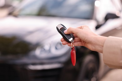 Photo of Woman holding car flip key near her vehicle outdoors, closeup