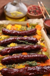 Baking tray with delicious smoked sausages and vegetables on table, closeup