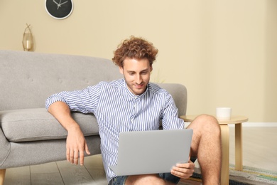 Photo of Young man with laptop sitting near sofa at home