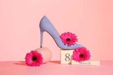 Photo of Composition with high heeled shoe and flowers on table against color background. International Women's Day