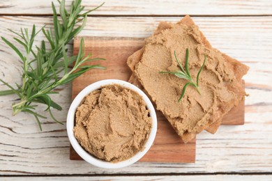 Photo of Crispy crackers with delicious meat pate and rosemary on white wooden table, flat lay