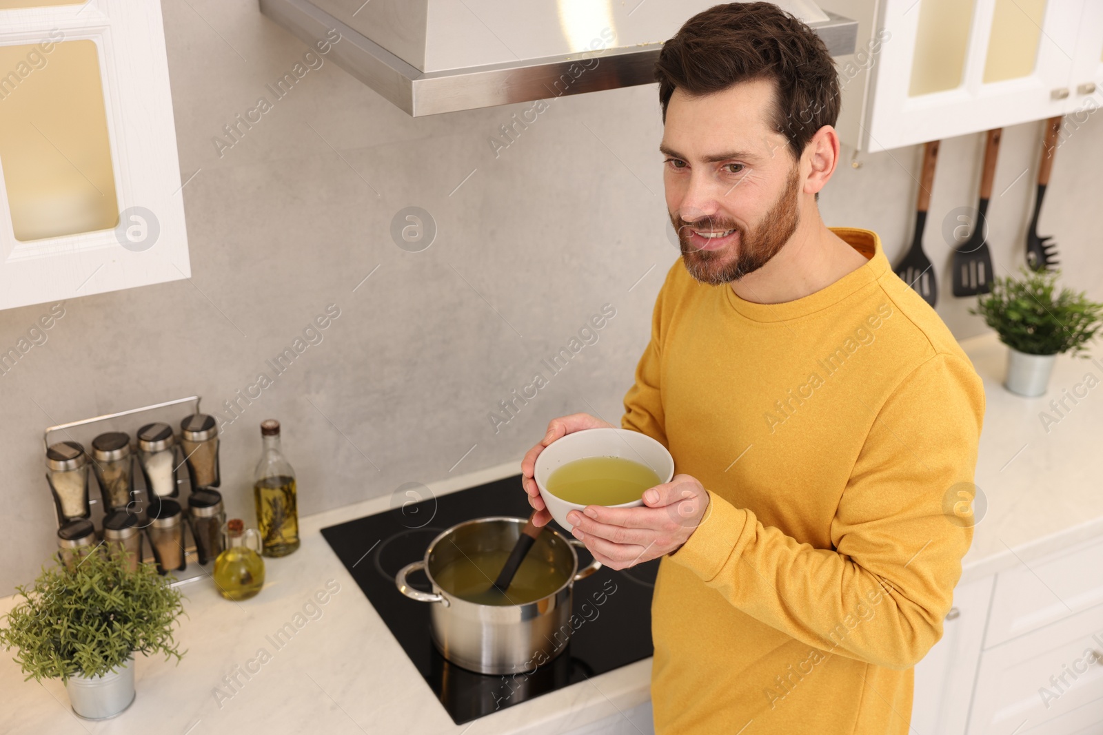Photo of Man with bowl of delicious soup in kitchen