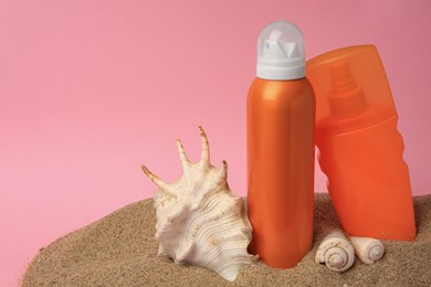 Sand with sunscreens and seashells against pink background, space for text. Sun protection care