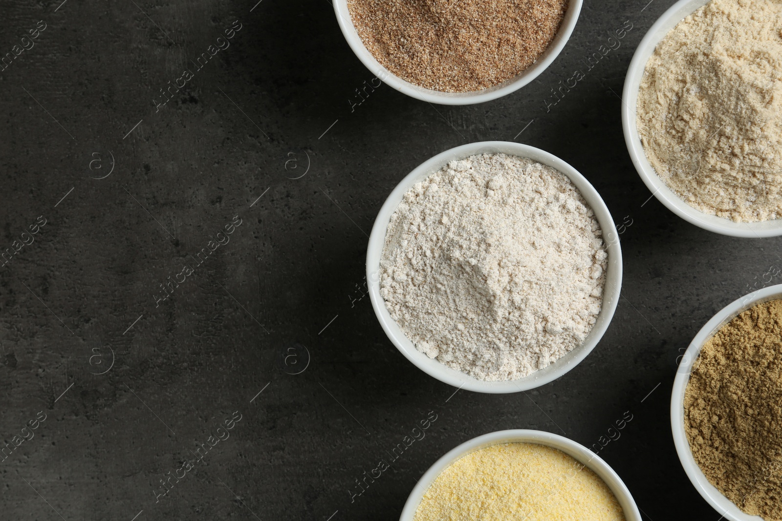 Photo of Bowls with different types of flour on grey background, top view. Space for text