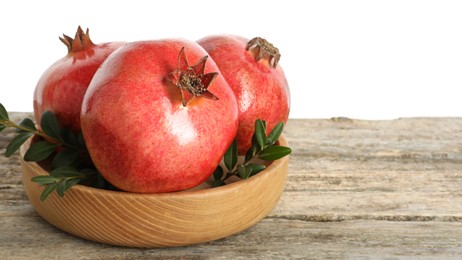 Photo of Fresh pomegranates and green leaves in bowl on wooden table against white background, space for text