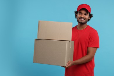 Happy courier with parcels on light blue background, space for text