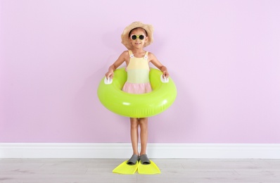 Photo of Cute little girl with inflatable ring wearing flippers near color wall