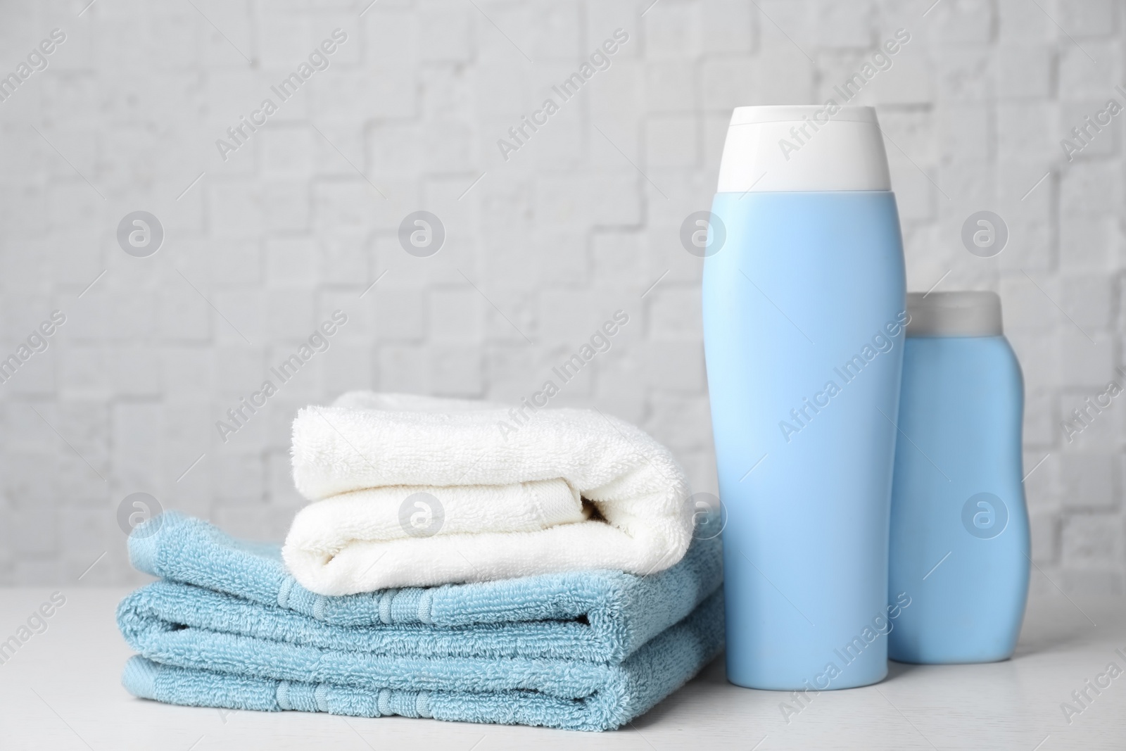 Photo of Folded towels and shampoo on table against white wall