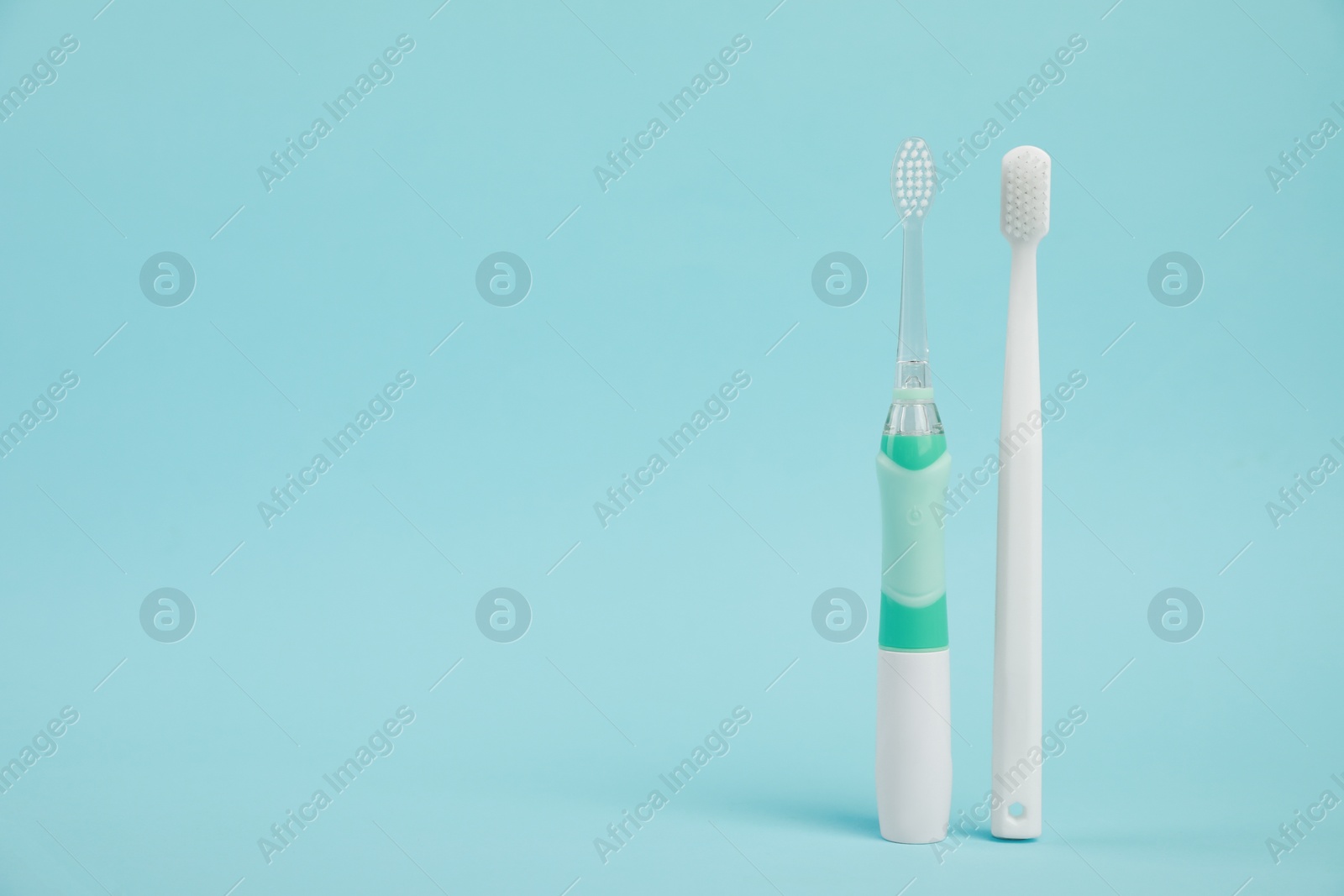 Photo of Electric and plastic toothbrushes on light blue background, space for text